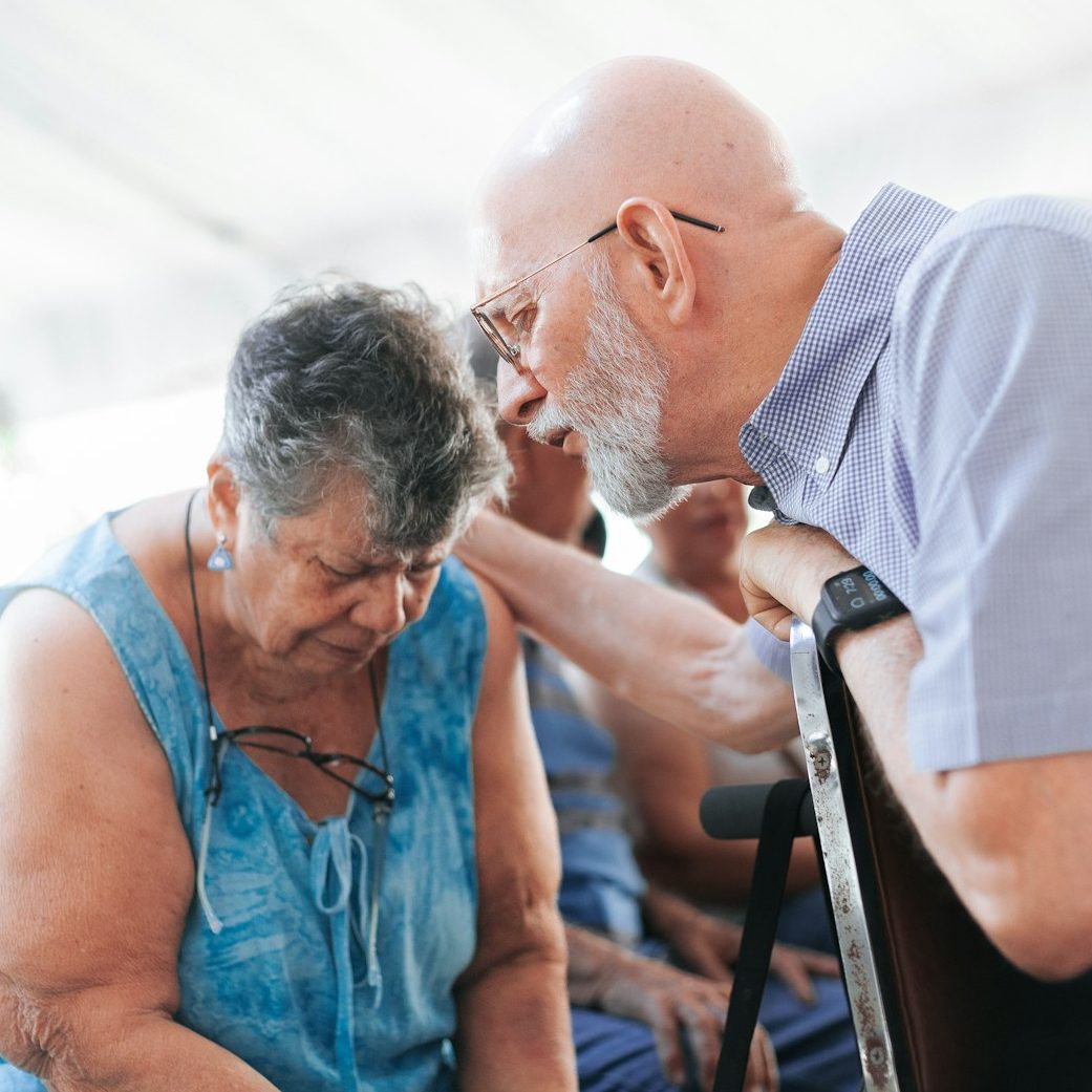 Ein einfühlsamer Betreuer spendet einer Seniorin Trost und Zuversicht durch eine beruhigende Geste im Alltag.